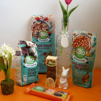 Schoko Kuchen, Knusper-Snack, Beeren-Crunch und riegel von DM Bio mit einem kleinen Hasen und einer Hyazinthe