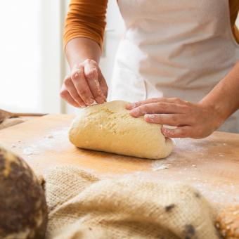 Frau mit weißer Schürze knetet einen glutenfreien Teig