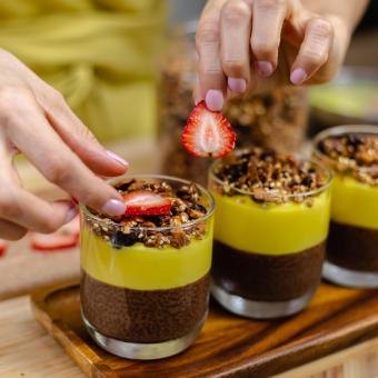 Eine Frau mit gelber Schürze dekoriert Desertgläser, die gefüllt sind mit einer braun-gelben Creme