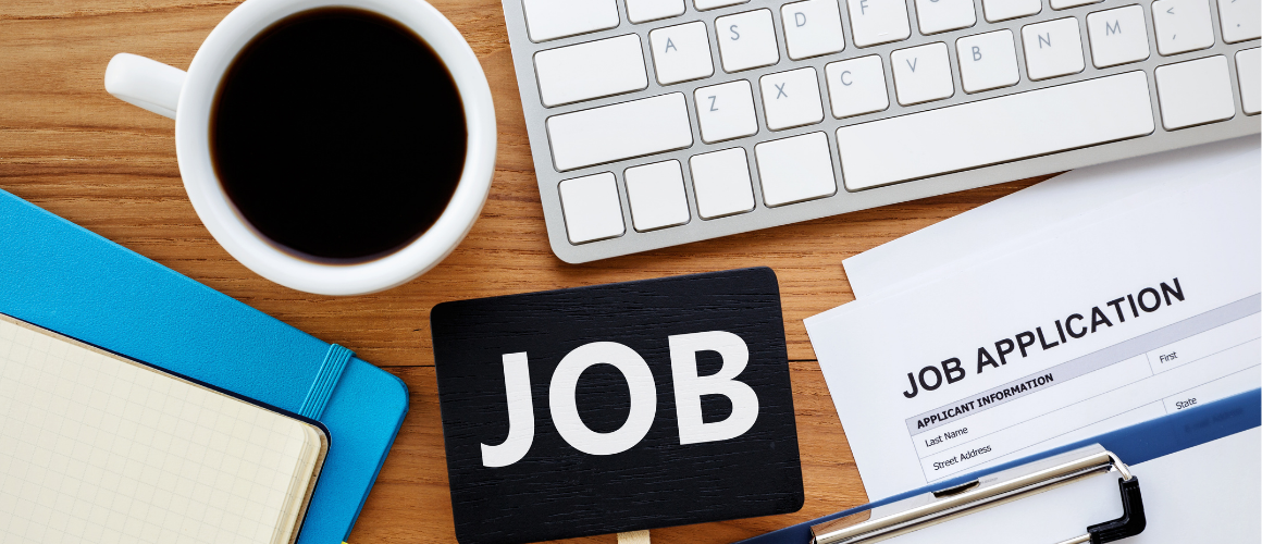 Schreibtisch auf dem eine Kaffeetasse mit kaffee steht, ein Laptop und ein Bewerbungsformular