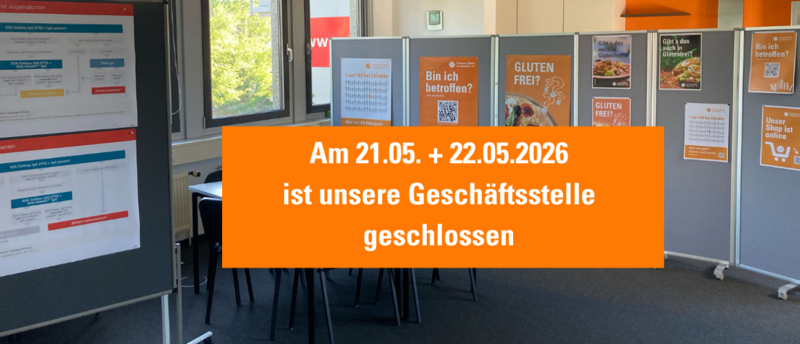 Innenaufnahme eines Besprechungsraumes der DZG mit Stellwänden und orangefarbenen Plakaten zum Thema Glutenfreiheit und Zöliakie. In der Bildmitte steht auf einem großen orangefarbenen Hinweis: „Am 21.05. + 22.05.2026 ist unsere Geschäftsstelle geschlossen.