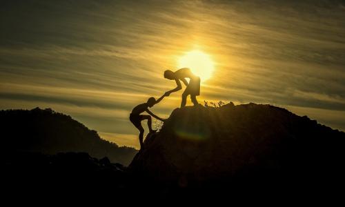 Mann hilft Mann auf Berggipfel im Sonnenuntergang
