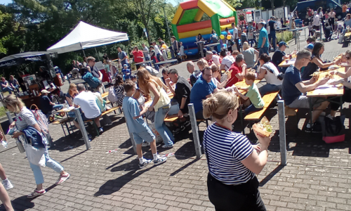 Kindererlebnistag 2025 Außengelände mit Hüpfburg, vielen Bänken und Tischen, Essensstände und relaxten Menschen- die Sonne scheint
