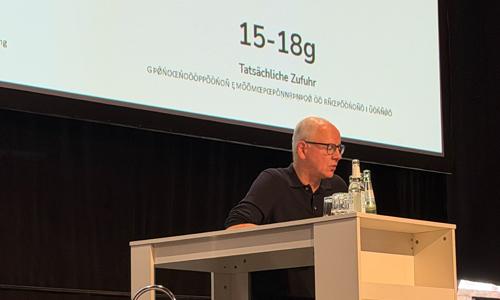 Dr. Söhnke Dammann sitzt am Rednerpult und gibt einen Überblick zum aktuellen Stand der Zöliakie im Jahr 2026. Dahinter sind auf der Leinwand Zahlen eingeblendet